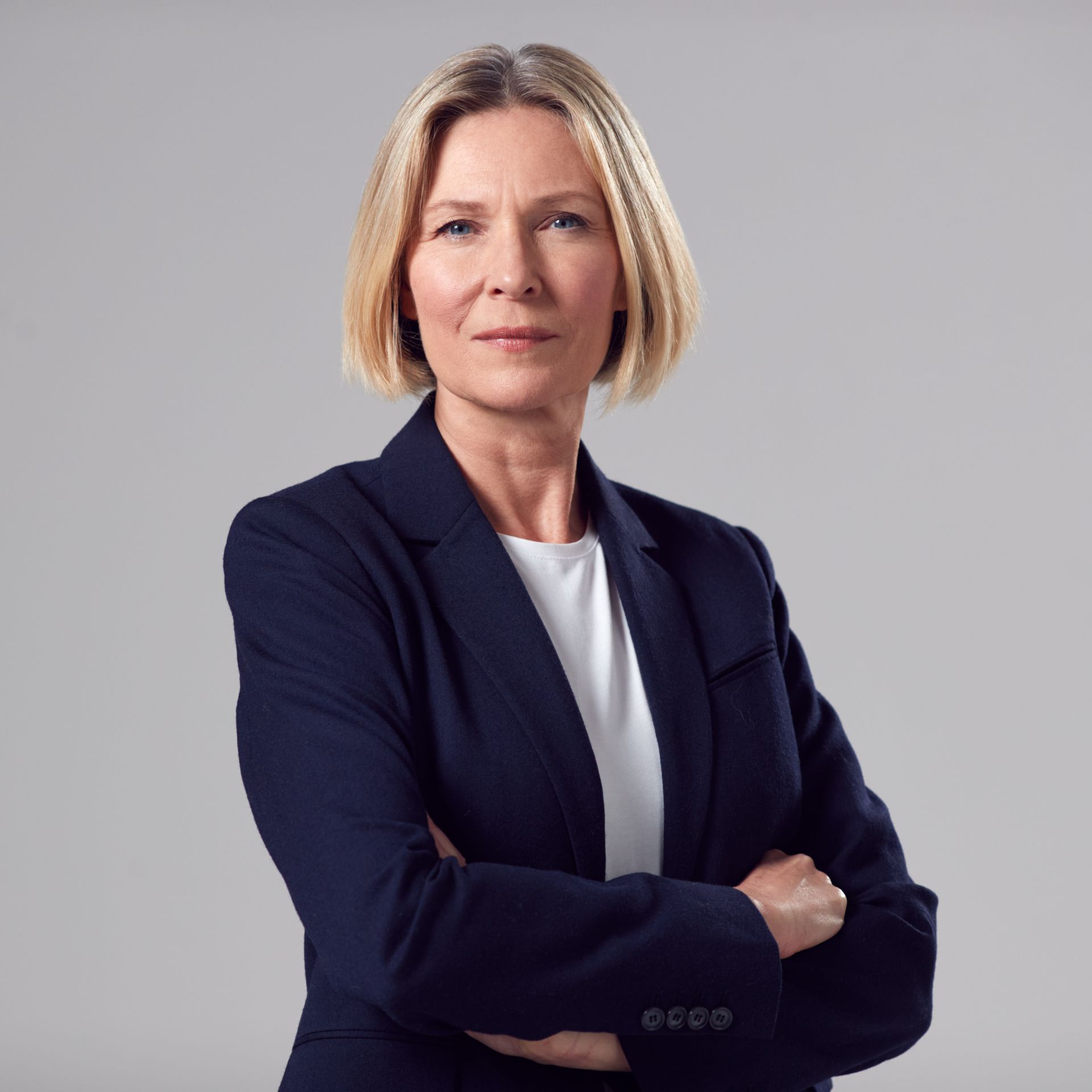 Professional woman with short blonde hair in a navy blazer stands confidently.
