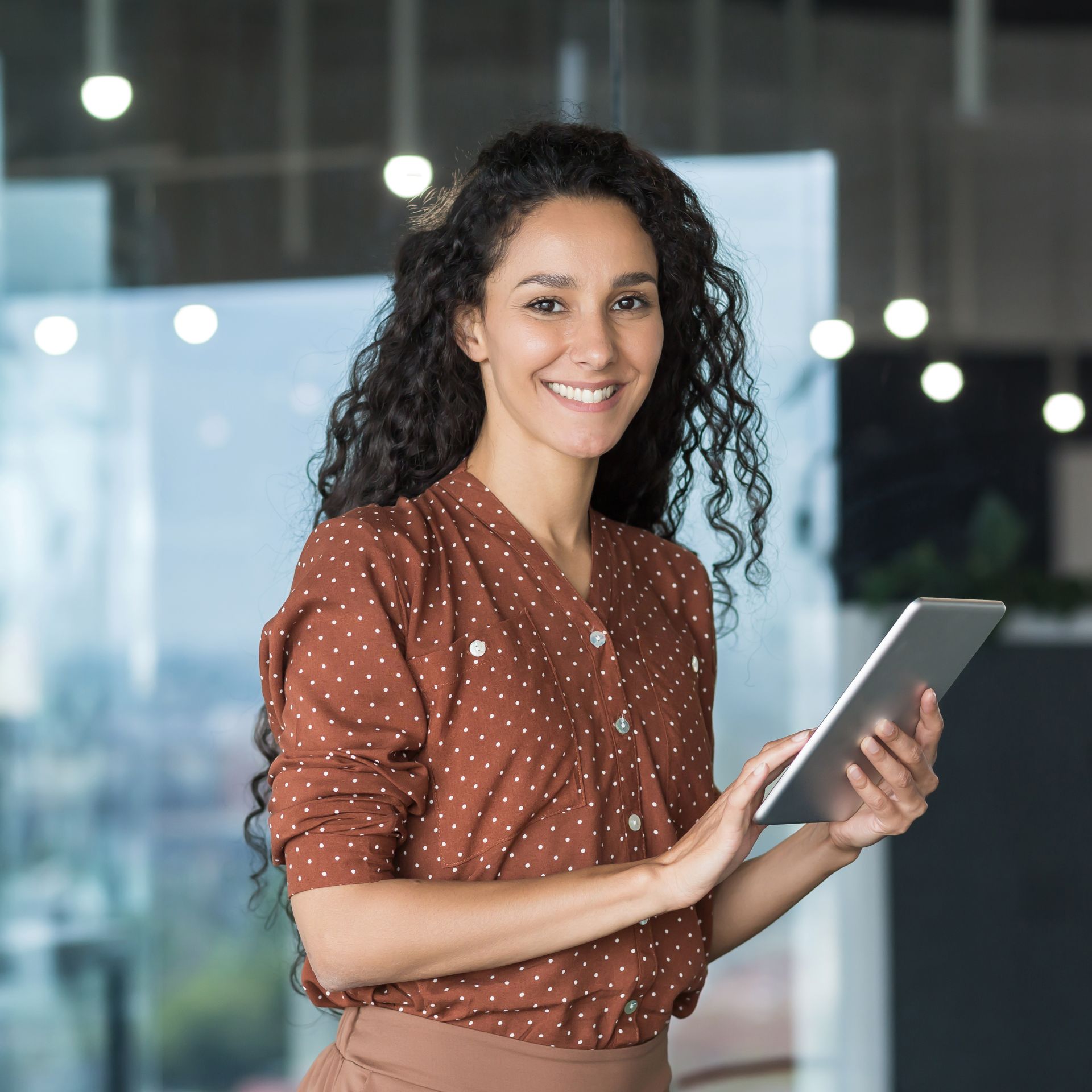 Smiling woman holding a tablet in a modern office setting.