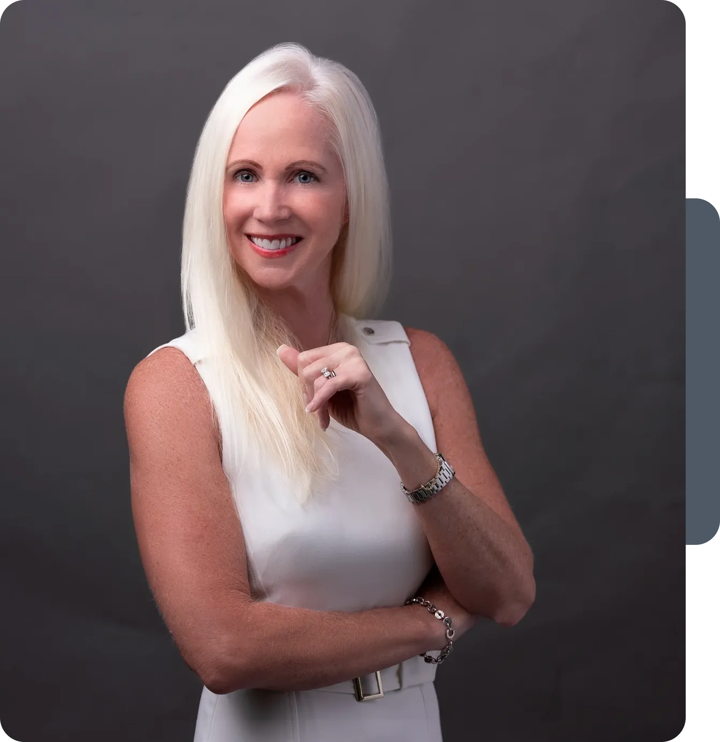 Smiling mature woman with long white hair, wearing a white sleeveless top.