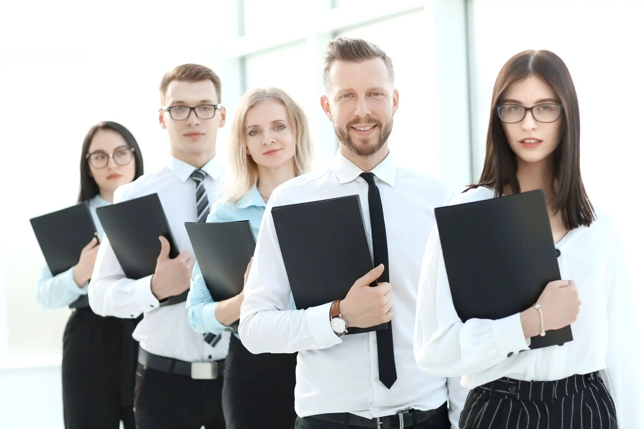 A group of five professionals holding black folders, standing in a row.