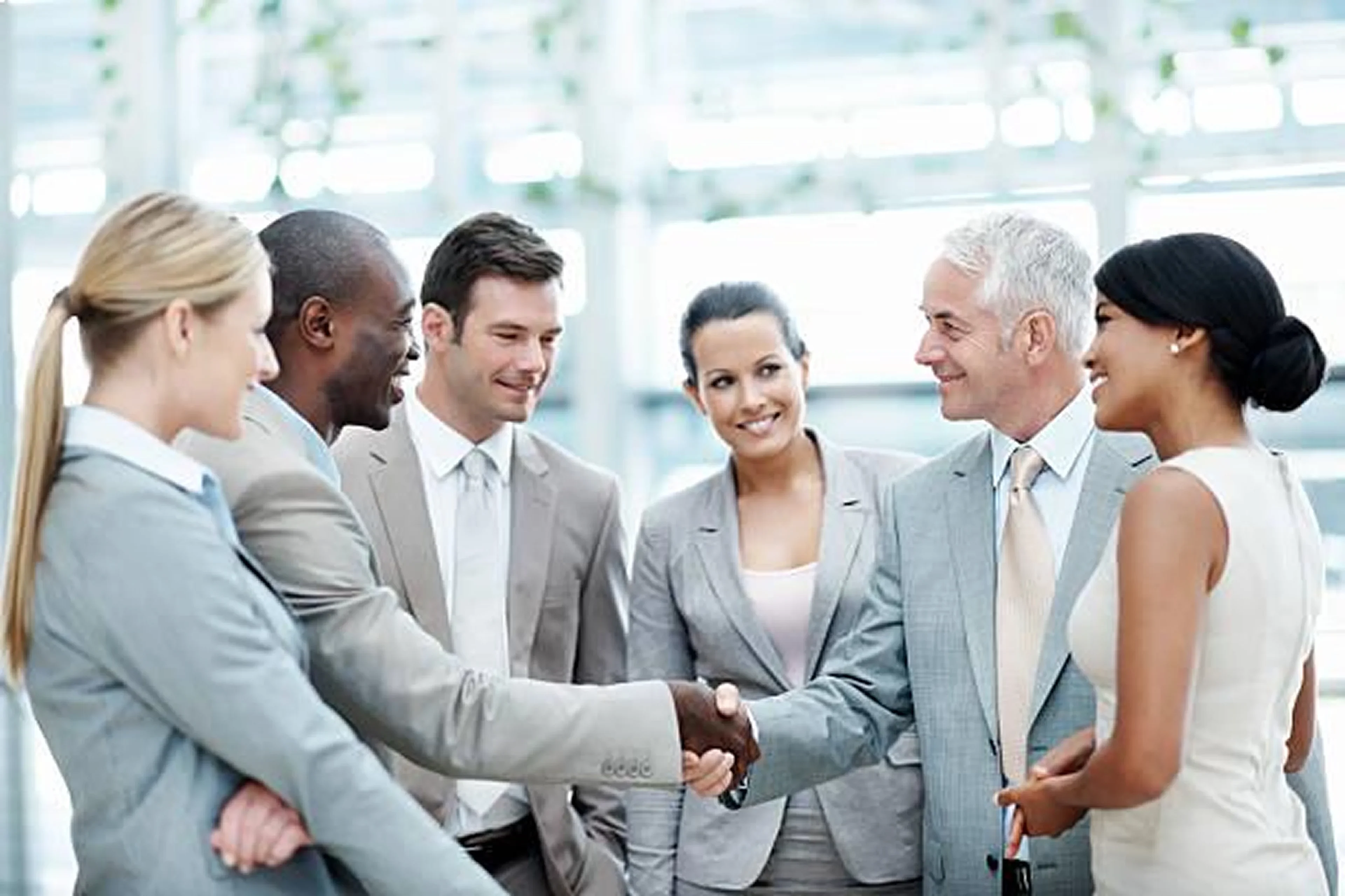 Business professionals shaking hands and smiling in a bright office.