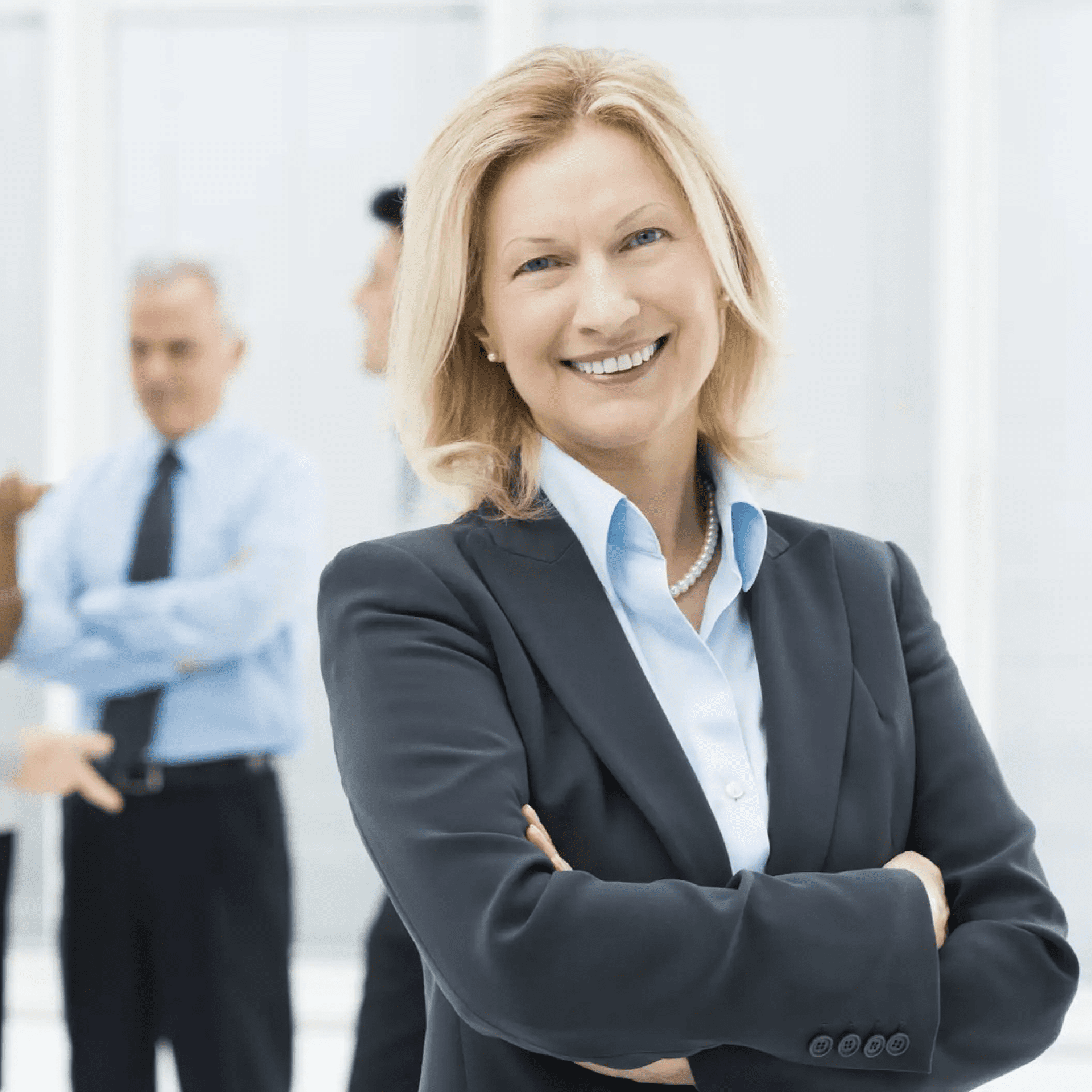 Confident businesswoman smiling with colleagues blurred in background.