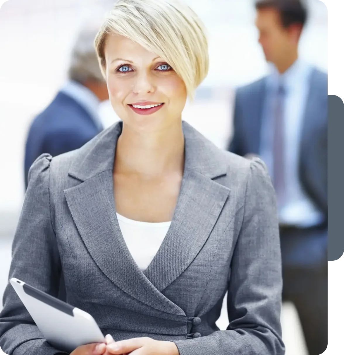 Confident businesswoman smiling with colleagues in the background.